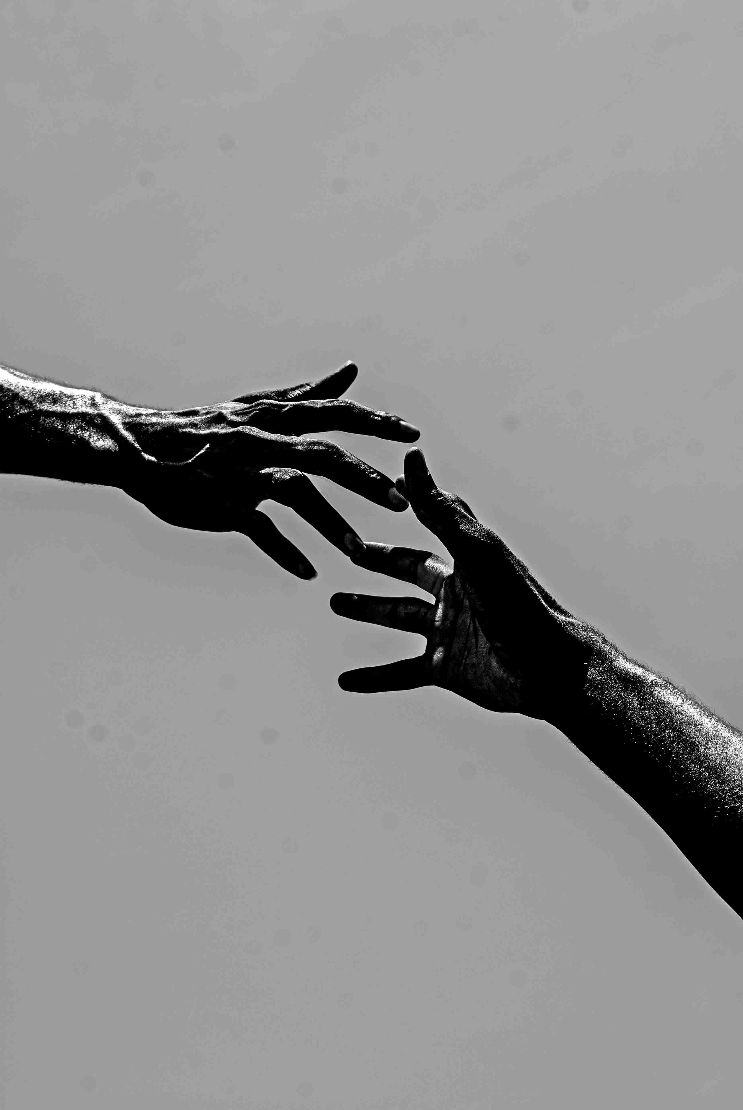 Two hands reaching for each other, greyscale.